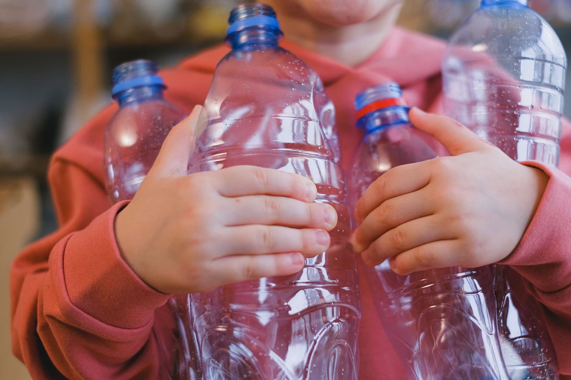 A person in a pink hoodie holding several empty clear plastic bottles.