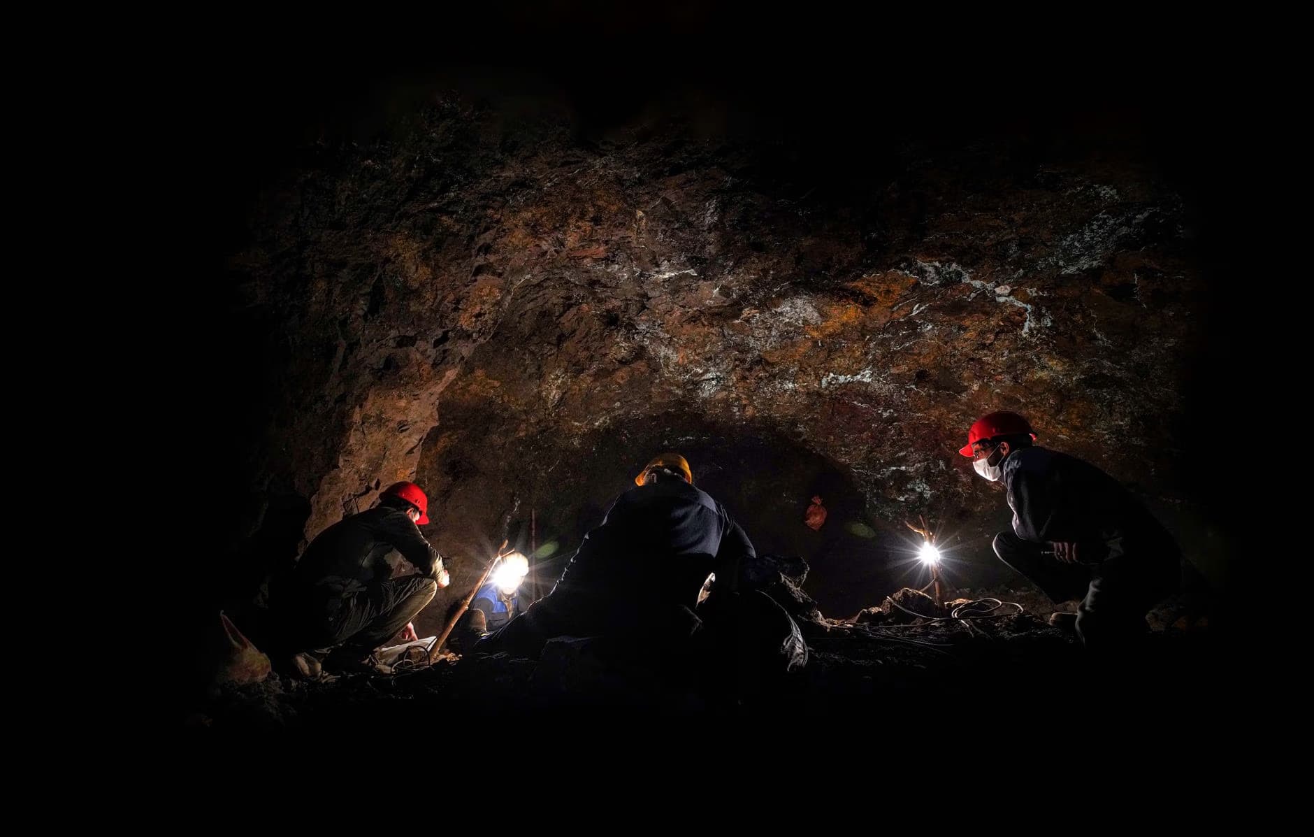 People wearing helmets and headlamps explore a dark underground cavern.