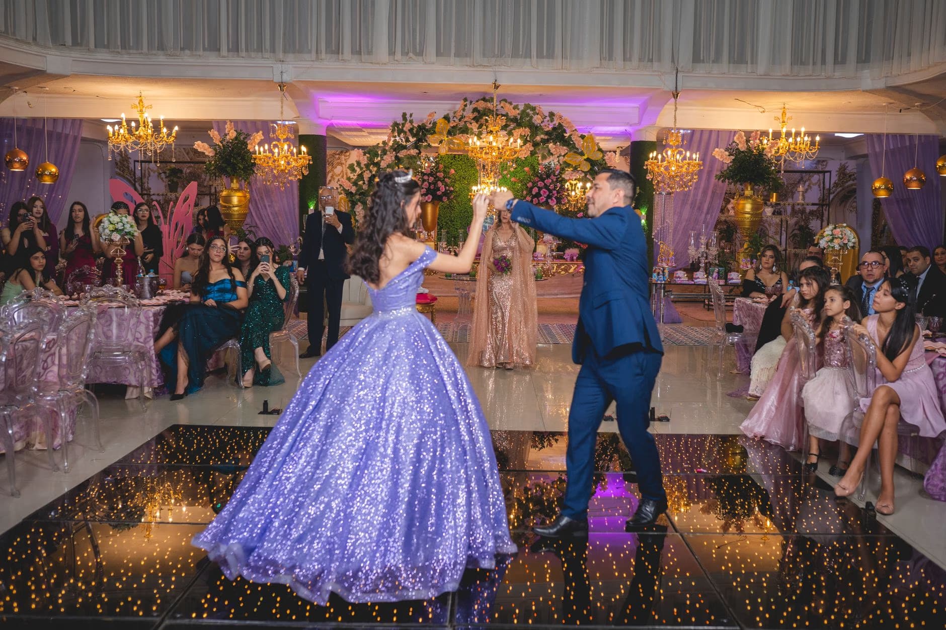 A young woman in a sparkly purple gown dances with a man at a formal party.