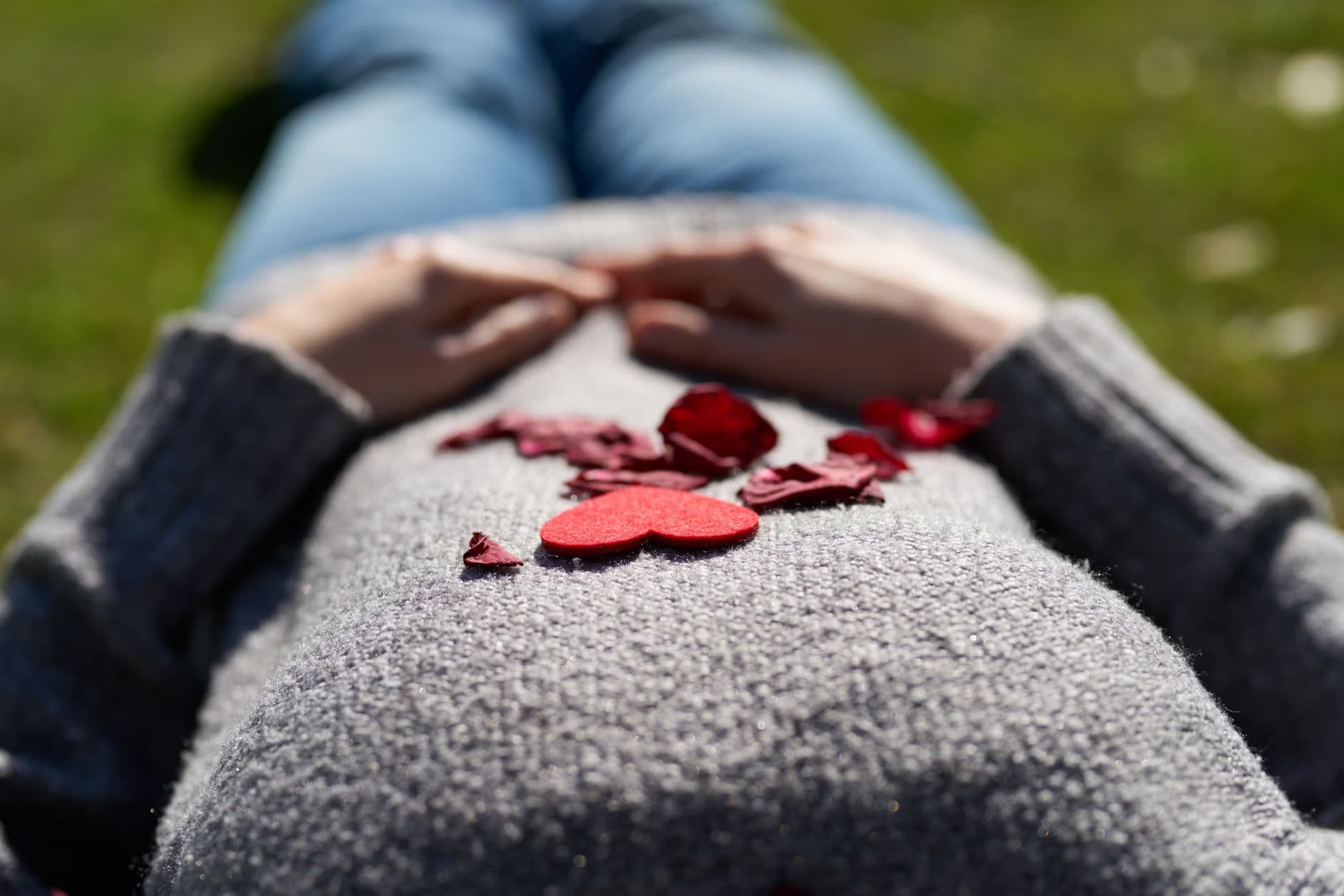 Person lying on grass with red heart shapes on their sweater over their chest.