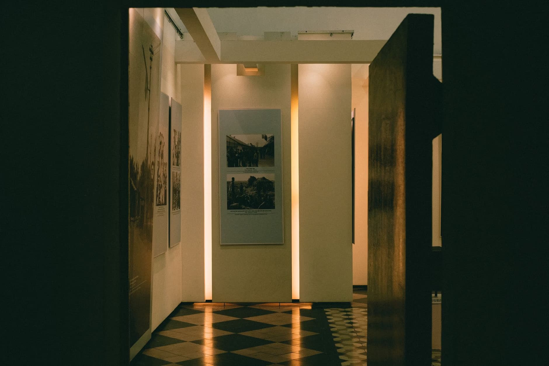 Wnętrze galerii sztuki z oświetlonymi ścianami i wyeksponowanymi w ramkach fotografiami.
