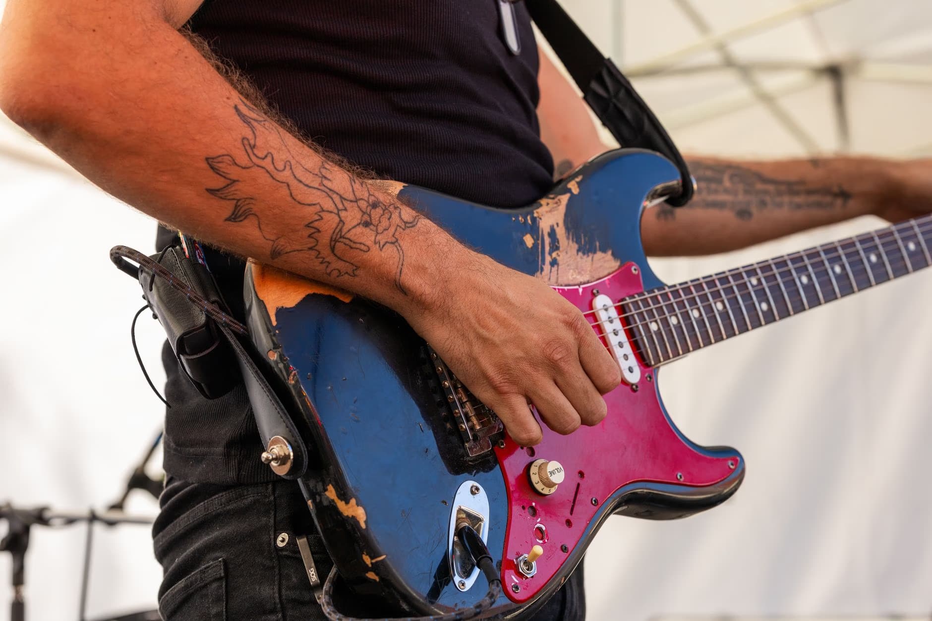 Close up of a musician playing a distressed blue electric guitar with a red pickguard on stage.