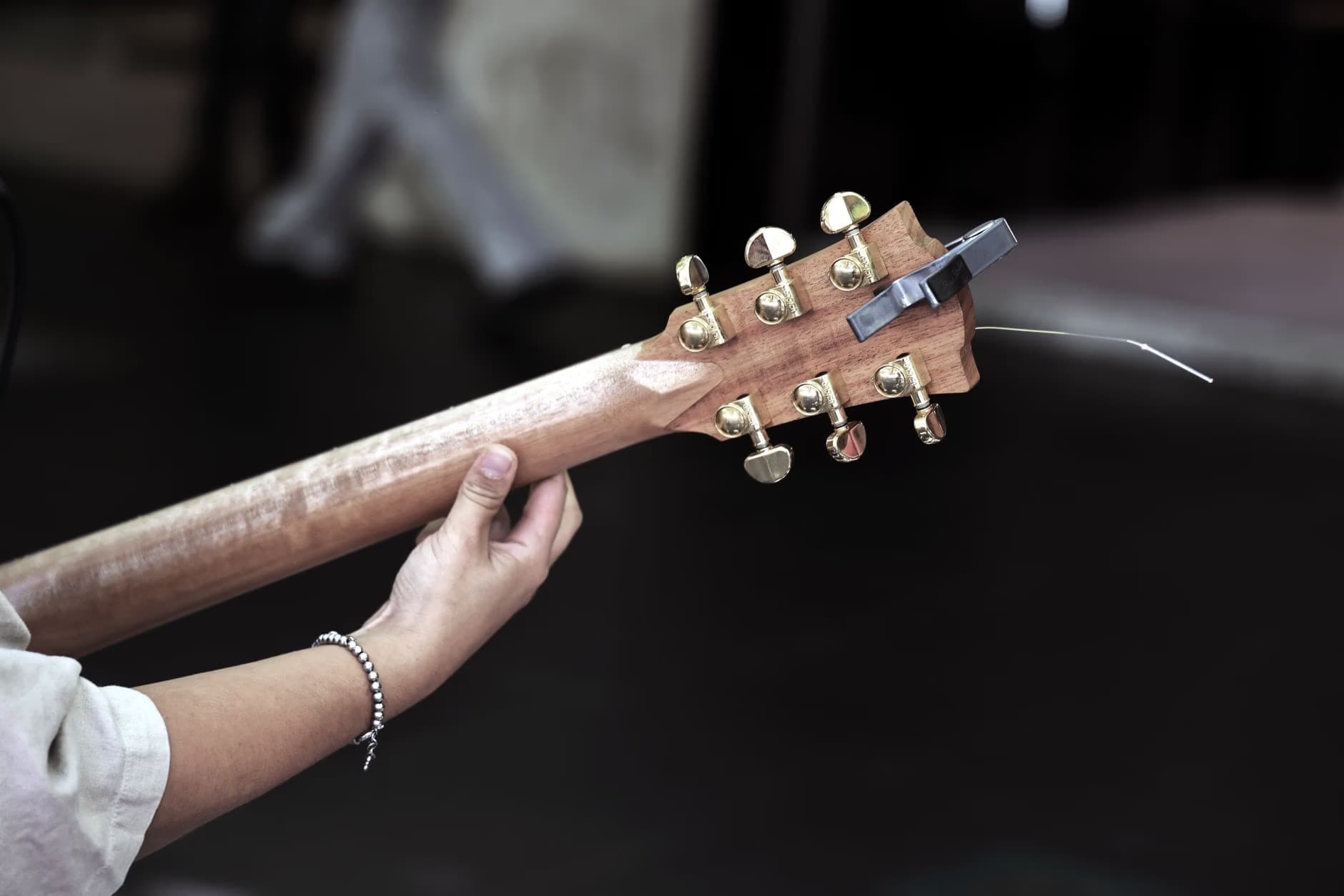 Close-up of a hand holding the neck of an acoustic guitar against a dark background.