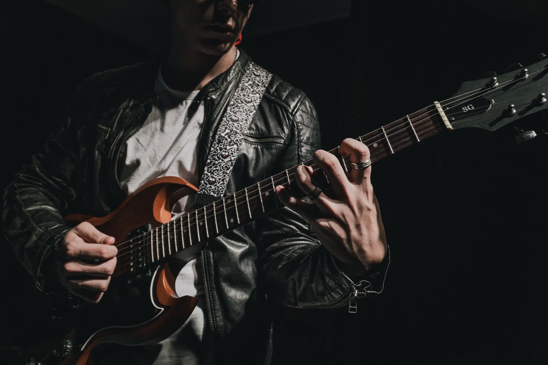 Musician playing a brown electric guitar while wearing a black leather jacket.