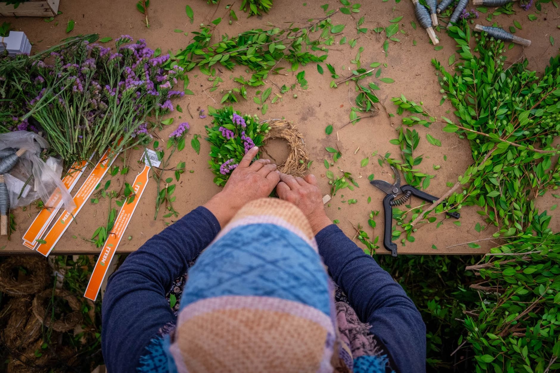 Eine Person aus der Vogelperspektive arrangiert Blumen und Grünpflanzen auf einem Holztisch.