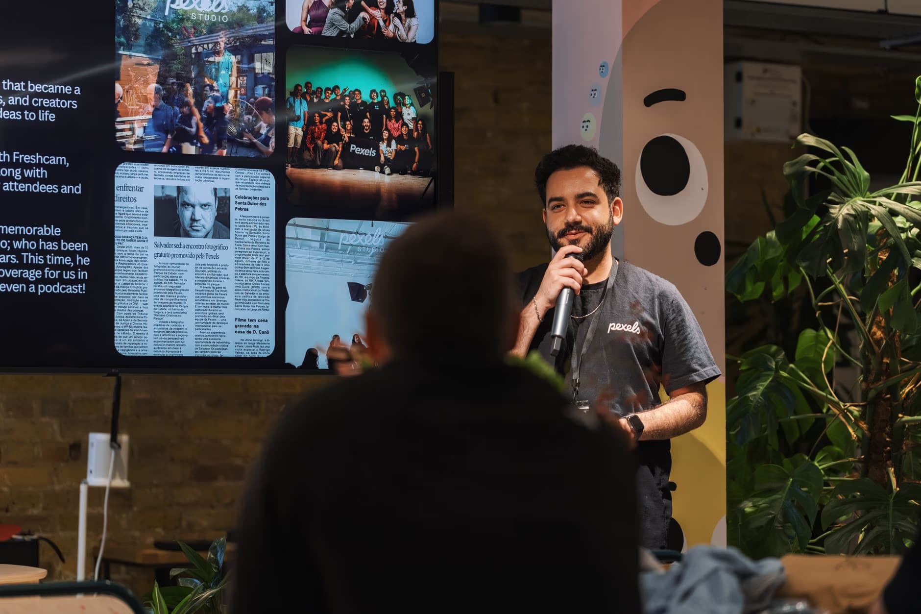 A man speaks into a microphone in front of a presentation screen with slides.