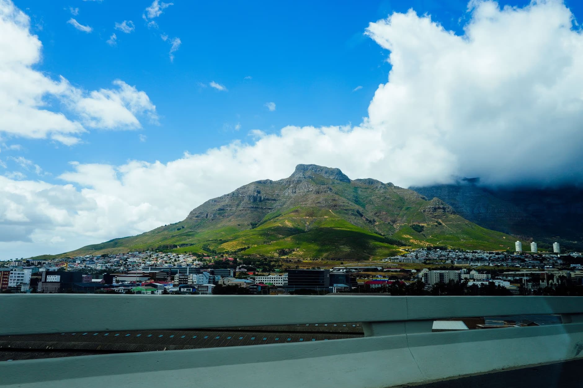 Table Mountain rises above a city under a bright blue sky with scattered clouds.