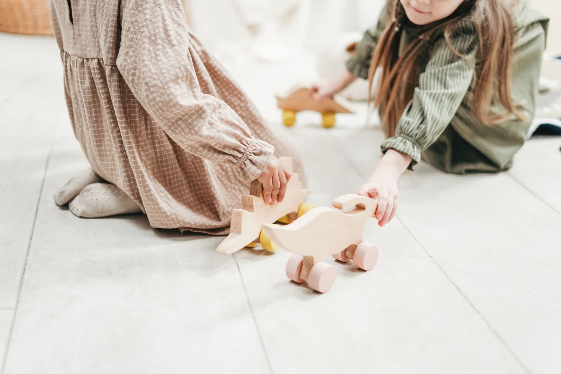 Two girls kneeling on a tiled floor playing with wooden toy ducks.