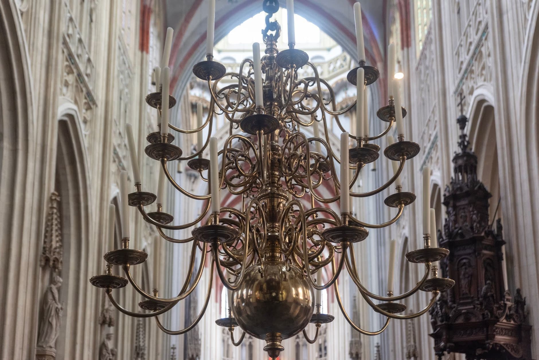 Ein großer, verzierter Messingkronleuchter hängt in einer hohen gotischen Kathedrale mit gewölbter Decke.