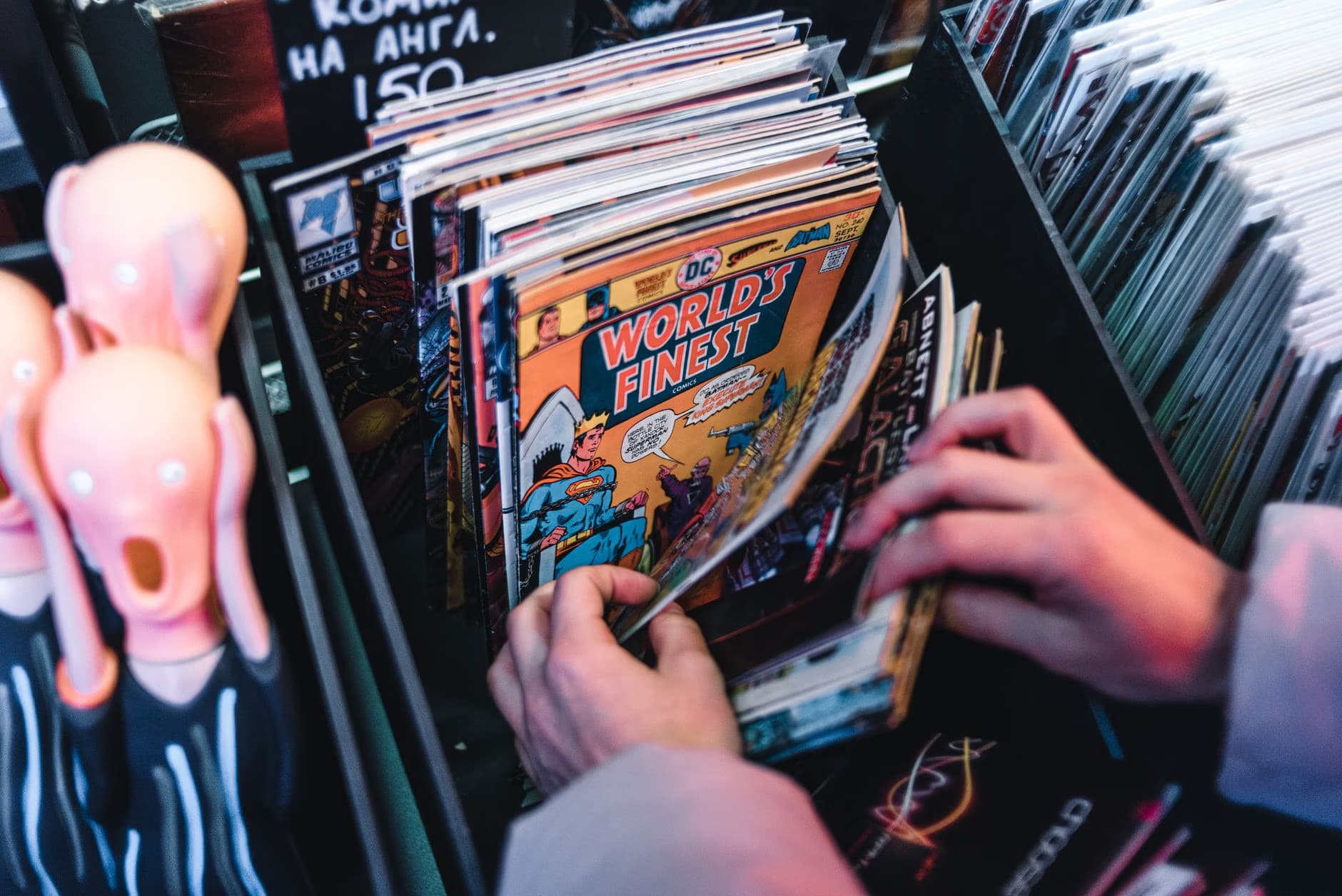Hands browsing through a bin of comic books at a shop.
