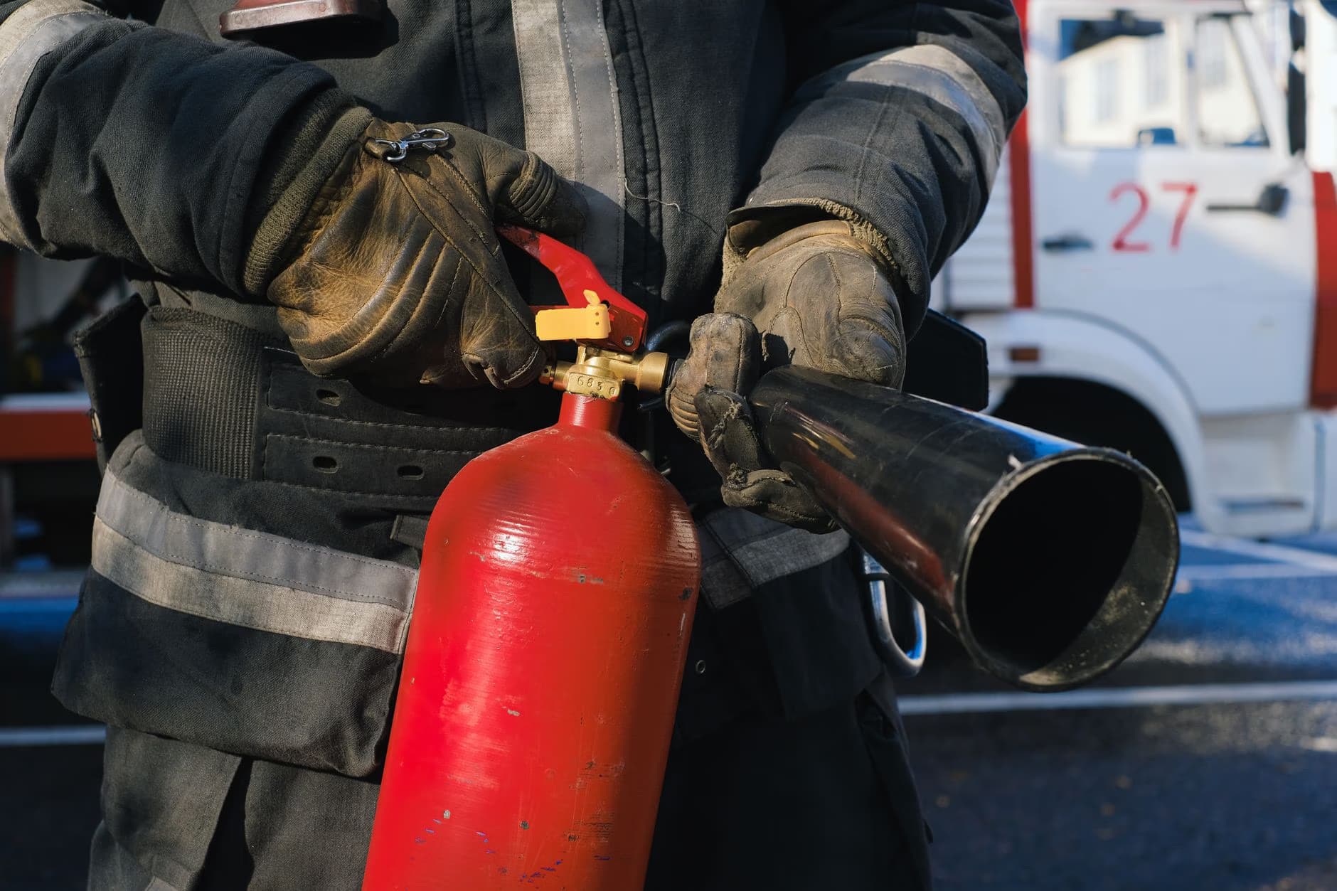 A firefighter in uniform wears protective gloves while holding a red fire extinguisher.