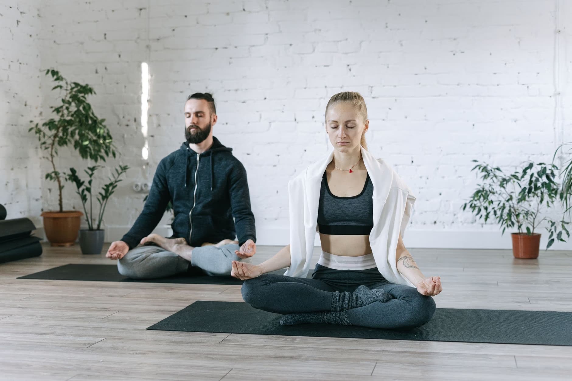 Ein Mann und eine Frau meditieren in einem hellen Yogastudio mit weißen Ziegelwänden.