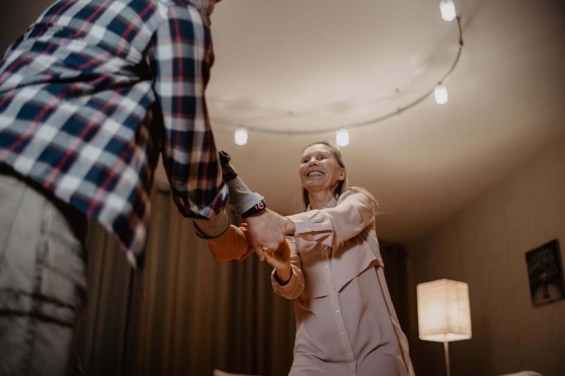 A couple holds hands and dances together in a warmly lit room.