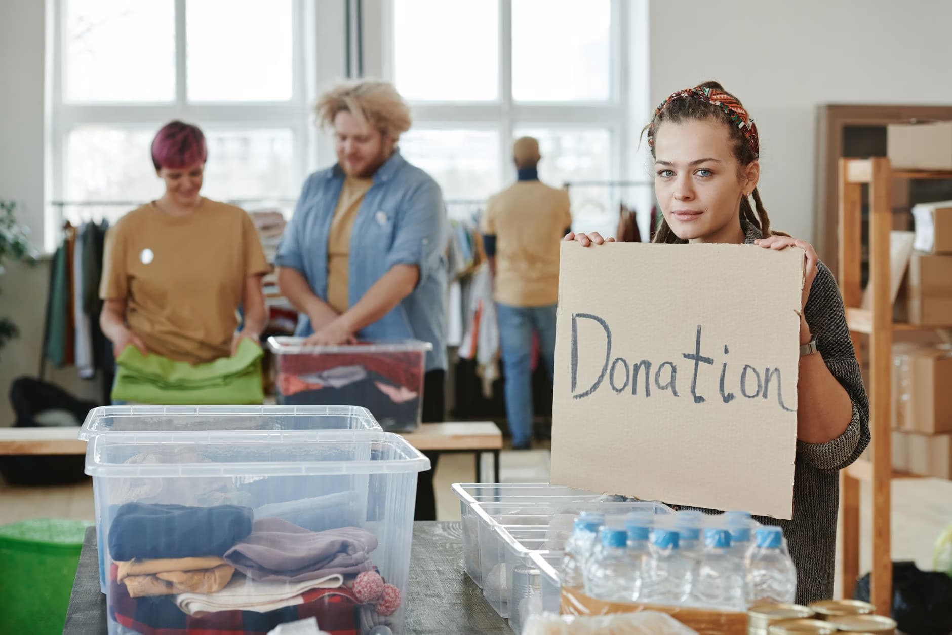 Kobieta trzyma znak z napisem Donation przed wolontariuszami sortującymi rzeczy w centrum darowizn.