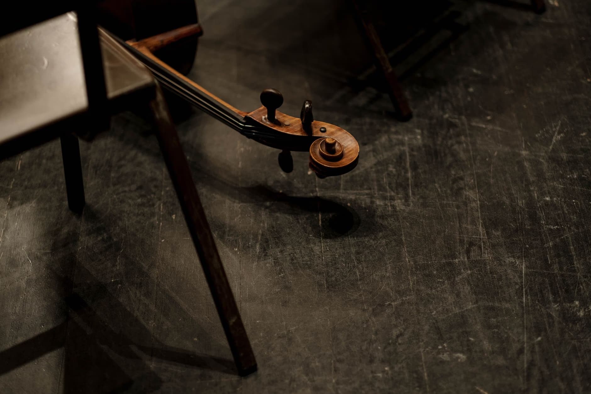 The scroll and pegbox of a string instrument rests on a wooden chair.
