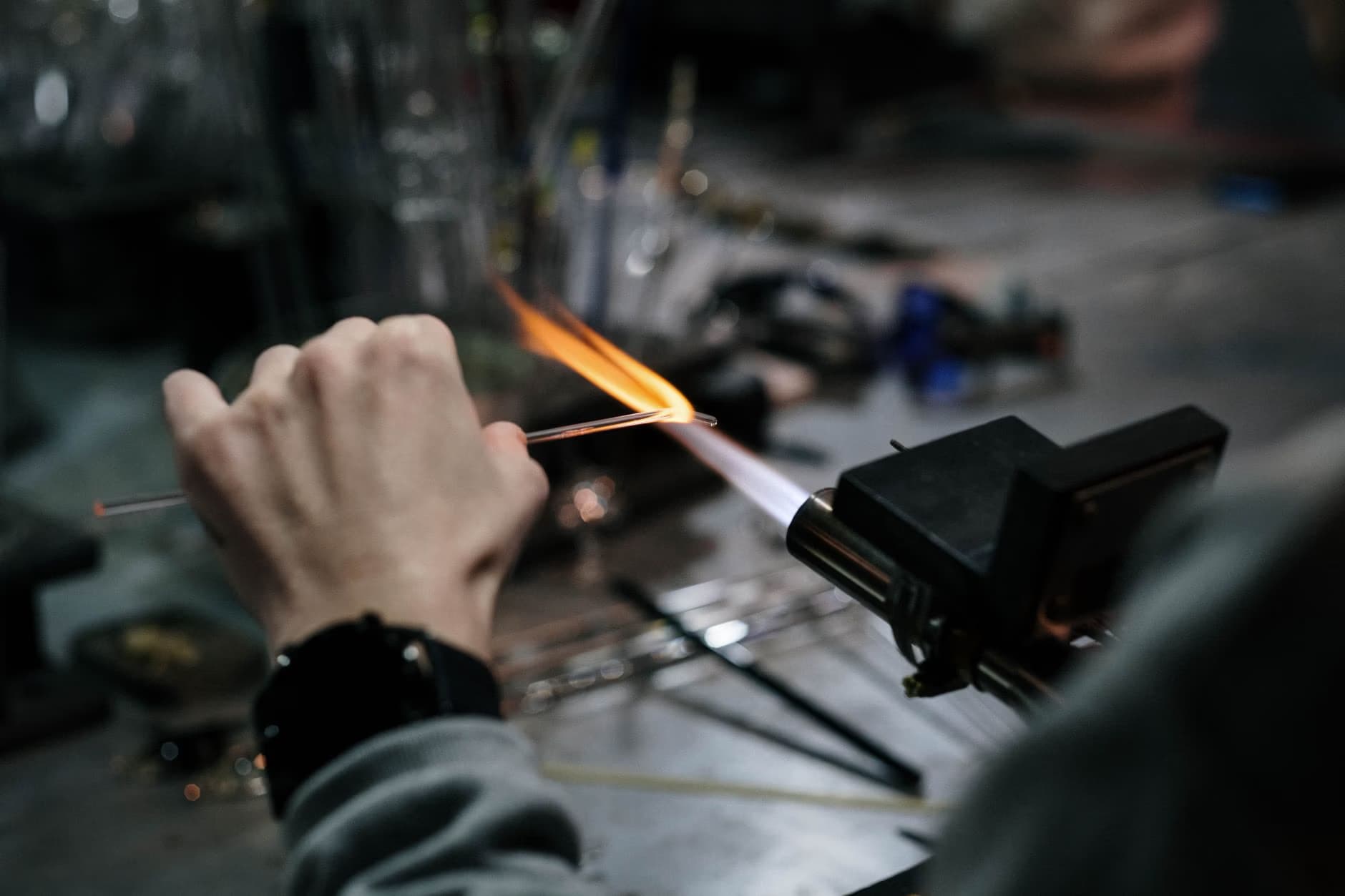 A close-up shot shows a person heating a glass rod in a torch flame.