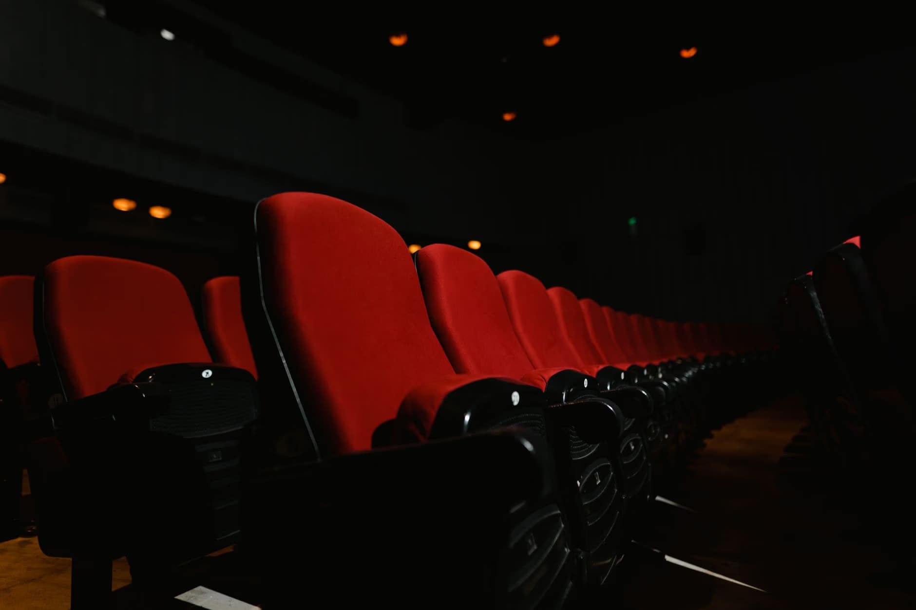 Eine Reihe leerer roter Kinostühle in einem schwach beleuchteten Theatersaal.
