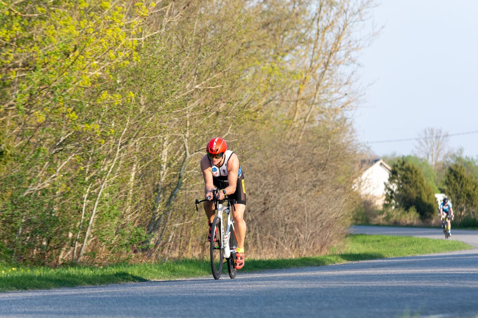Cyklista v červené helmě jede na silničním kole po cestě lemované stromy.