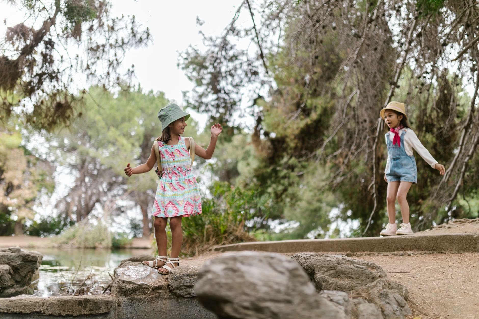 Two young girls in sun hats play happily together near a small forest stream.