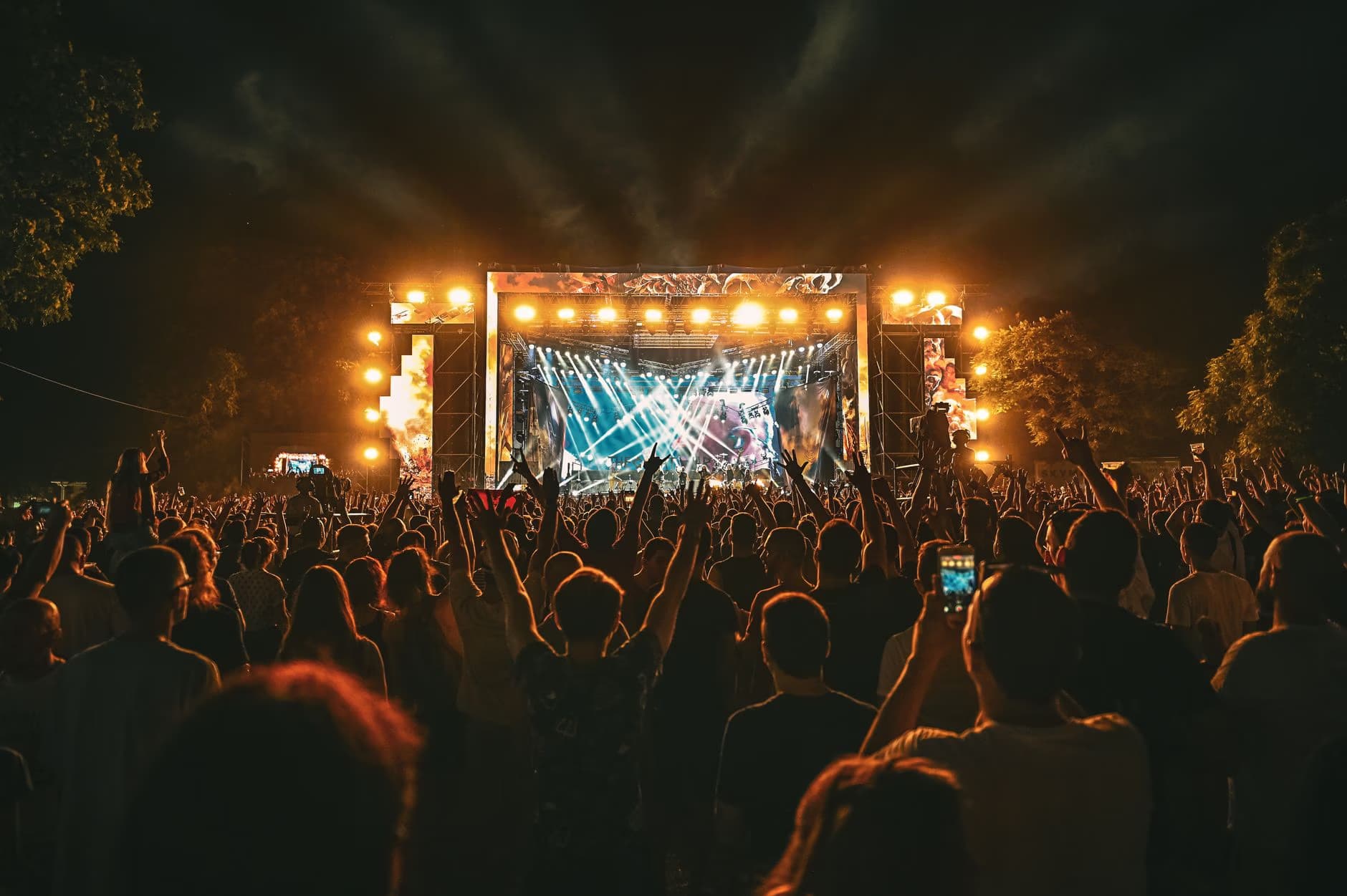 A crowded music festival at night with an illuminated stage and laser lights.