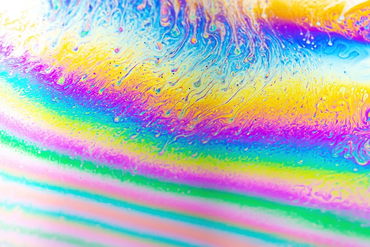 Macro view of iridescent, colorful swirling patterns on a soap bubble surface.