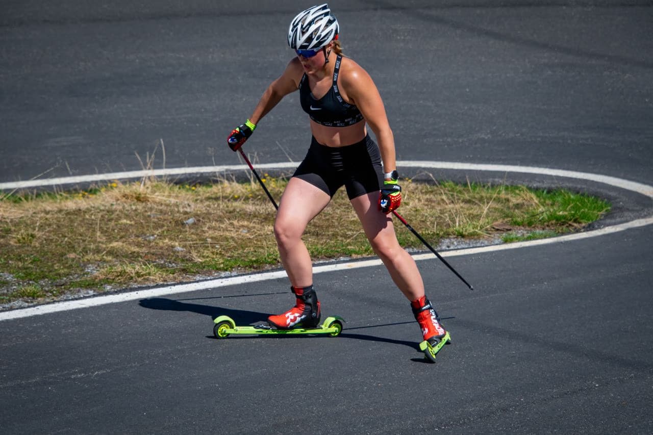 A woman wearing a sports outfit and helmet roller skiing on an outdoor asphalt track.