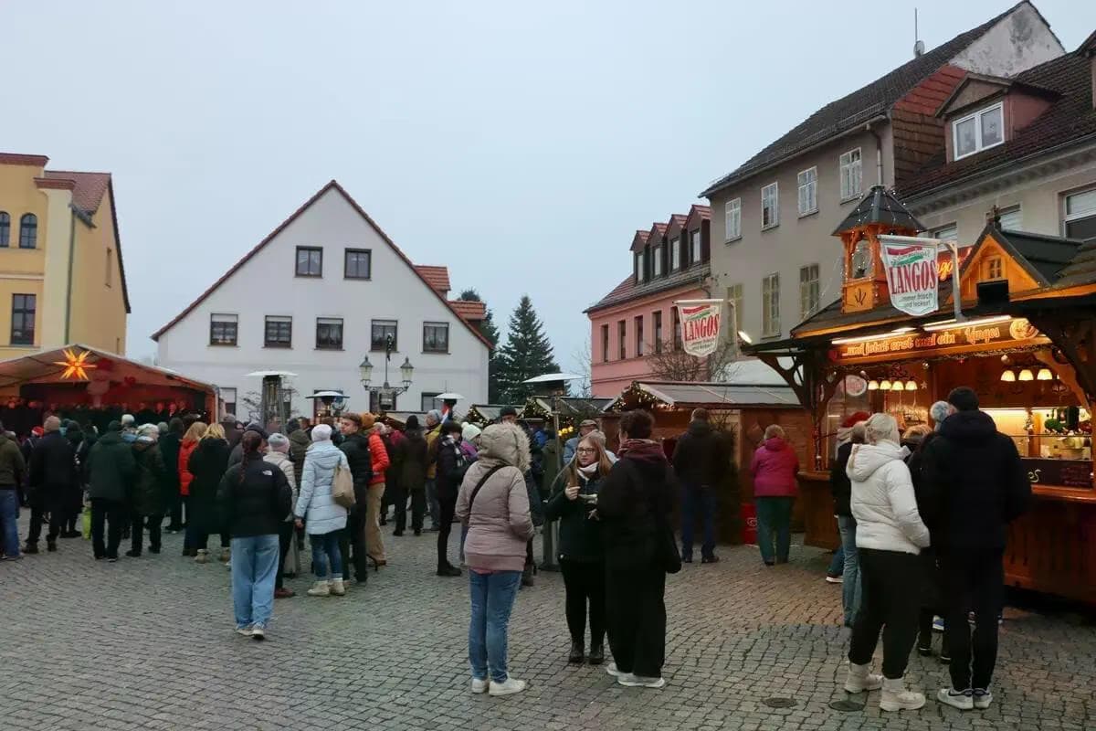Tłum ludzi spacerujący po rynku wypełnionym drewnianymi straganami.
