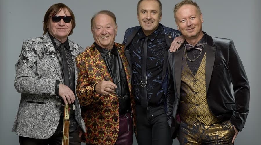 Four men in patterned formal jackets and suits pose together against a plain grey background.