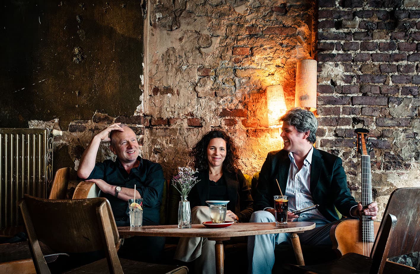 Three people sit around a table in a dimly lit room with an exposed brick wall.