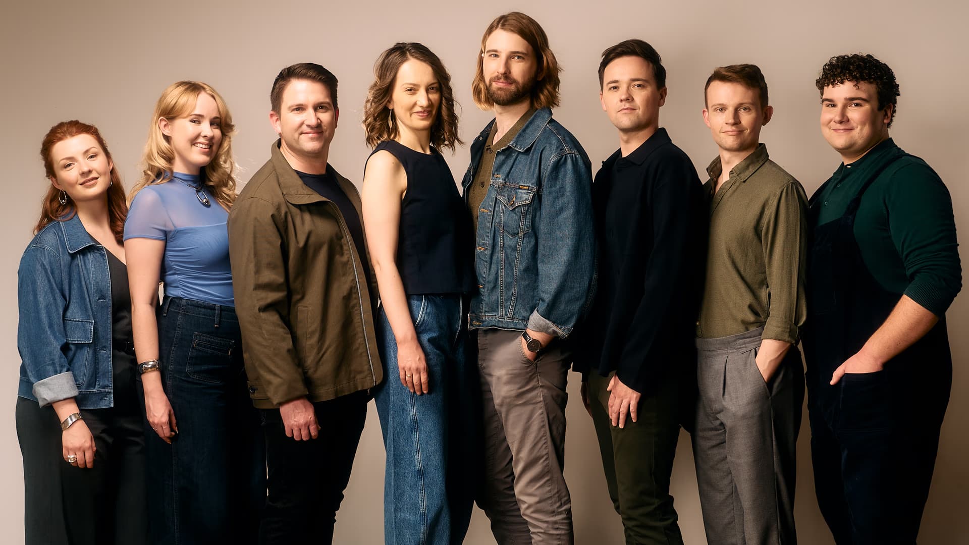 A group of eight young adults stands in a line against a plain neutral background.