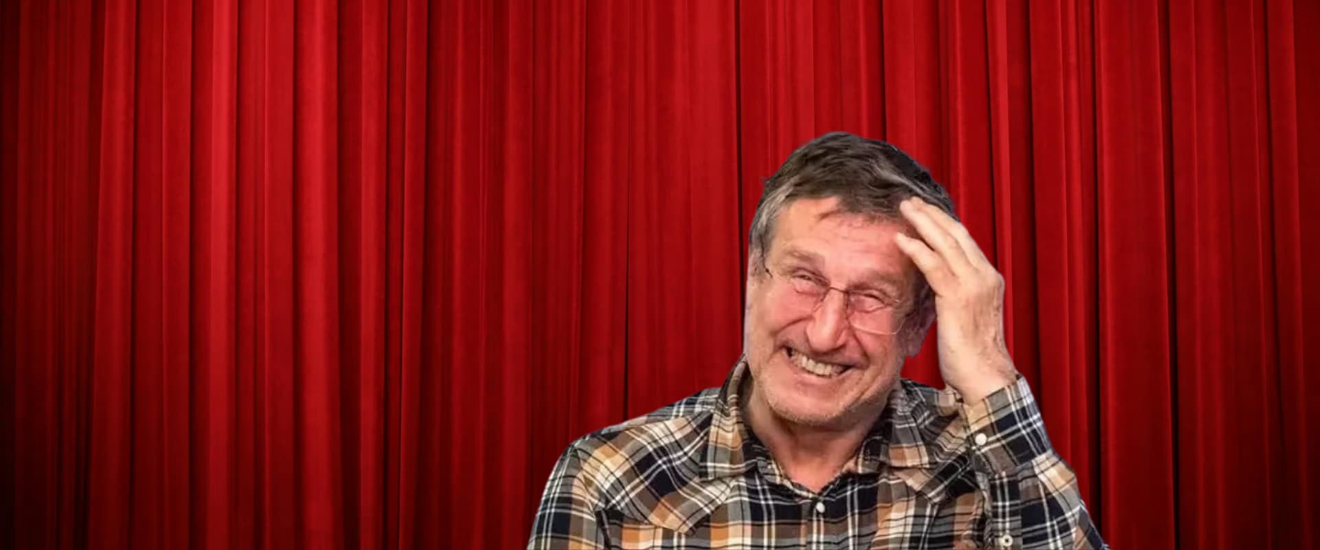 Älterer Mann im karierten Hemd lächelt und fasst sich vor einem roten Vorhang an die Haare.