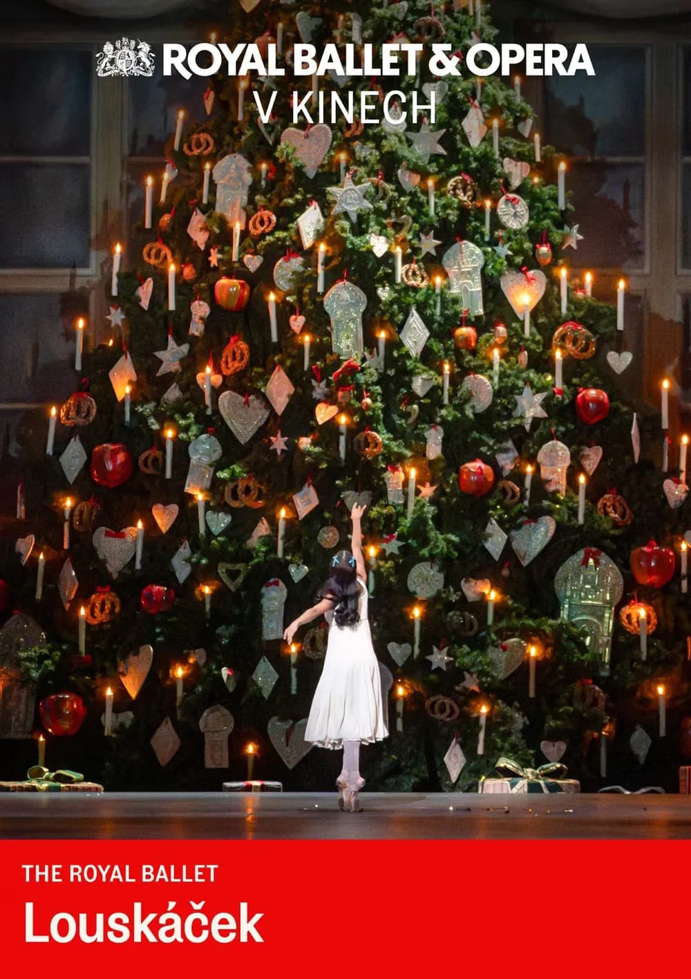 A dancer in a white dress performs before a large Christmas tree on a stage.