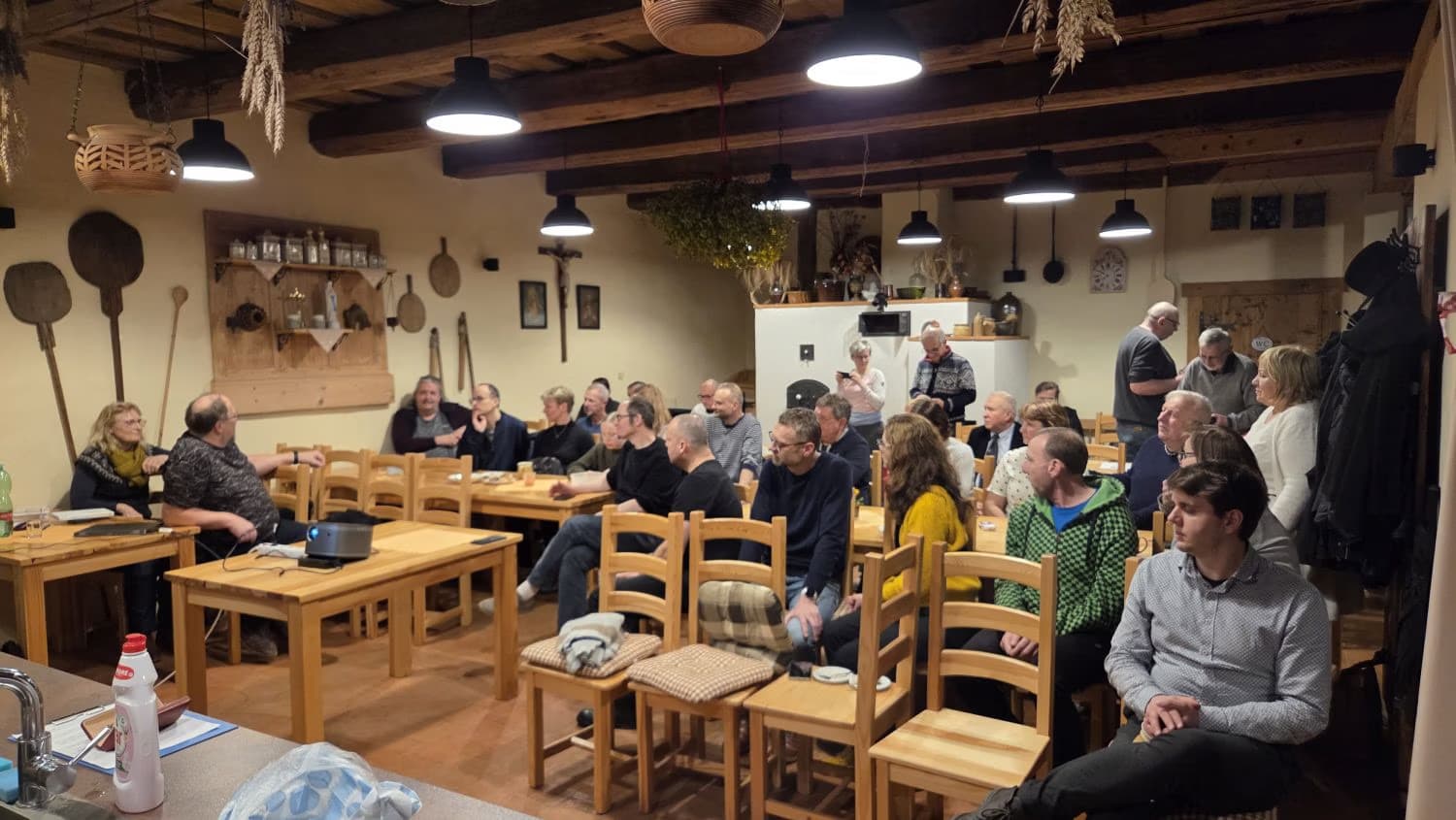 A group of people are gathered sitting at wooden tables inside a rustic, warmly lit room.