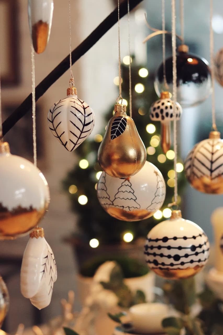 Various black and white Christmas ornaments hang from a branch before a blurred tree.