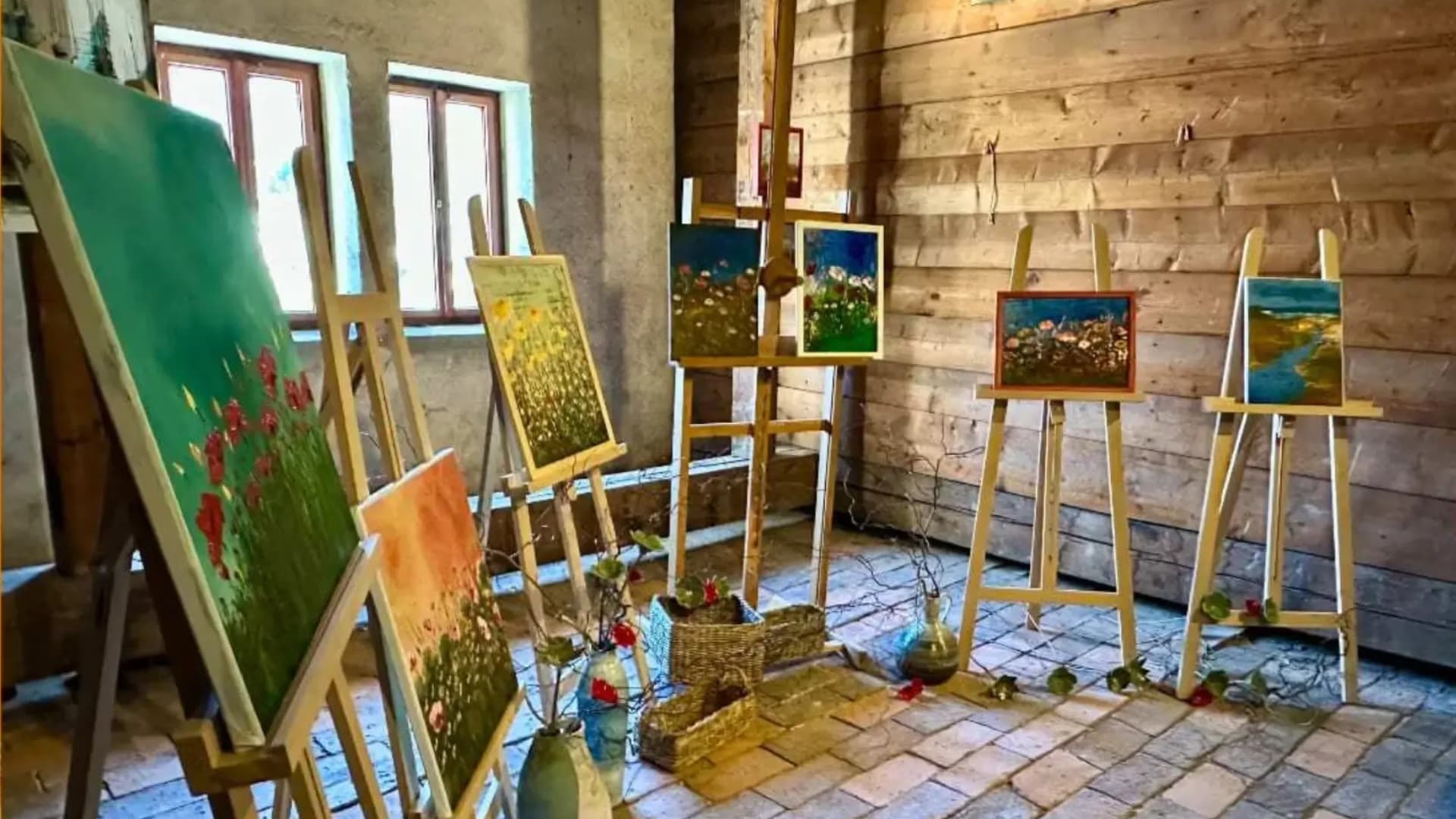 Artworks displayed on wooden easels inside a rustic room with wooden walls.