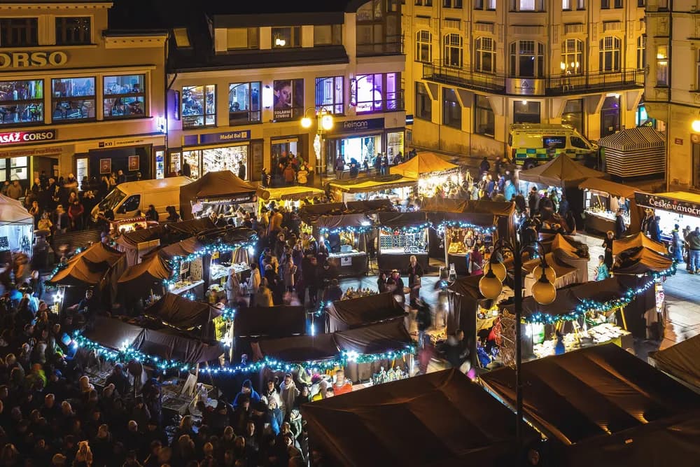 Belebter Außenmarkt mit beleuchteten Holzbuden auf einem historischen Stadtplatz bei Nacht.