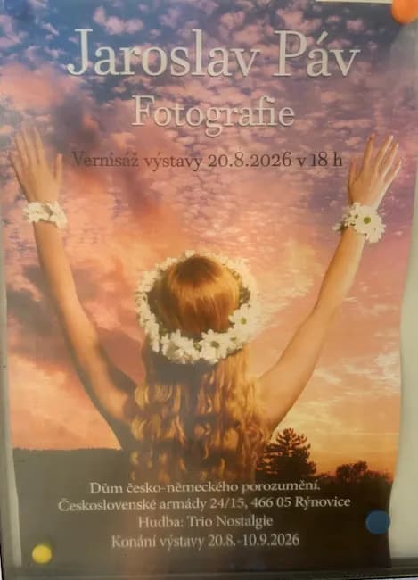 A woman with a floral wreath raises her arms towards a sunset sky on an exhibition poster.