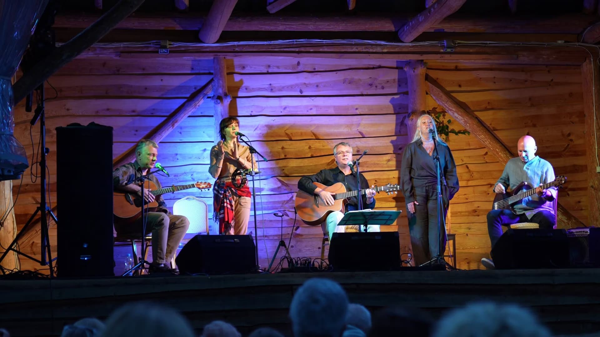 A band performs live on a stage with a rustic wooden wall background.