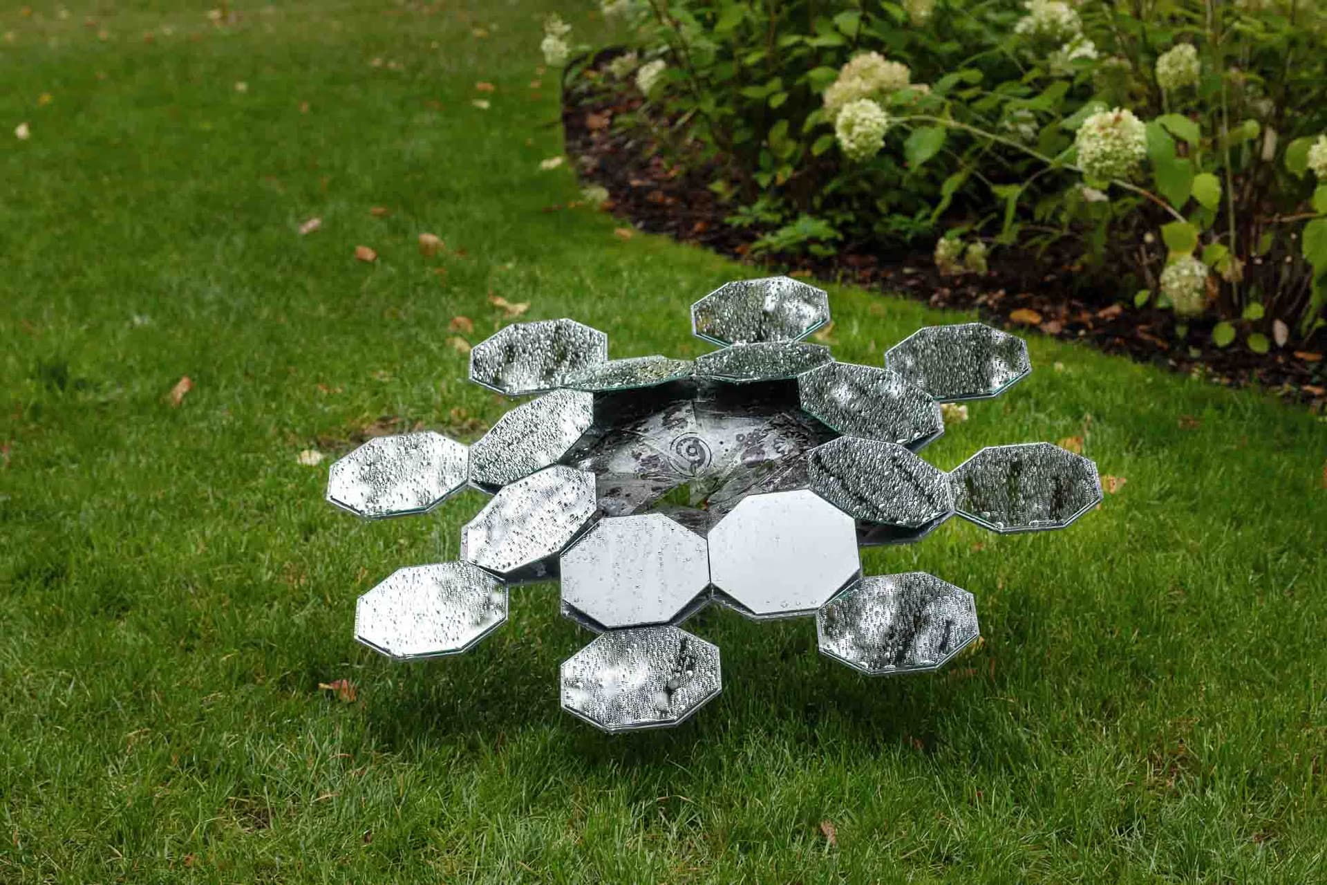 A geometric sculpture made of small mirror segments sits on a green lawn.