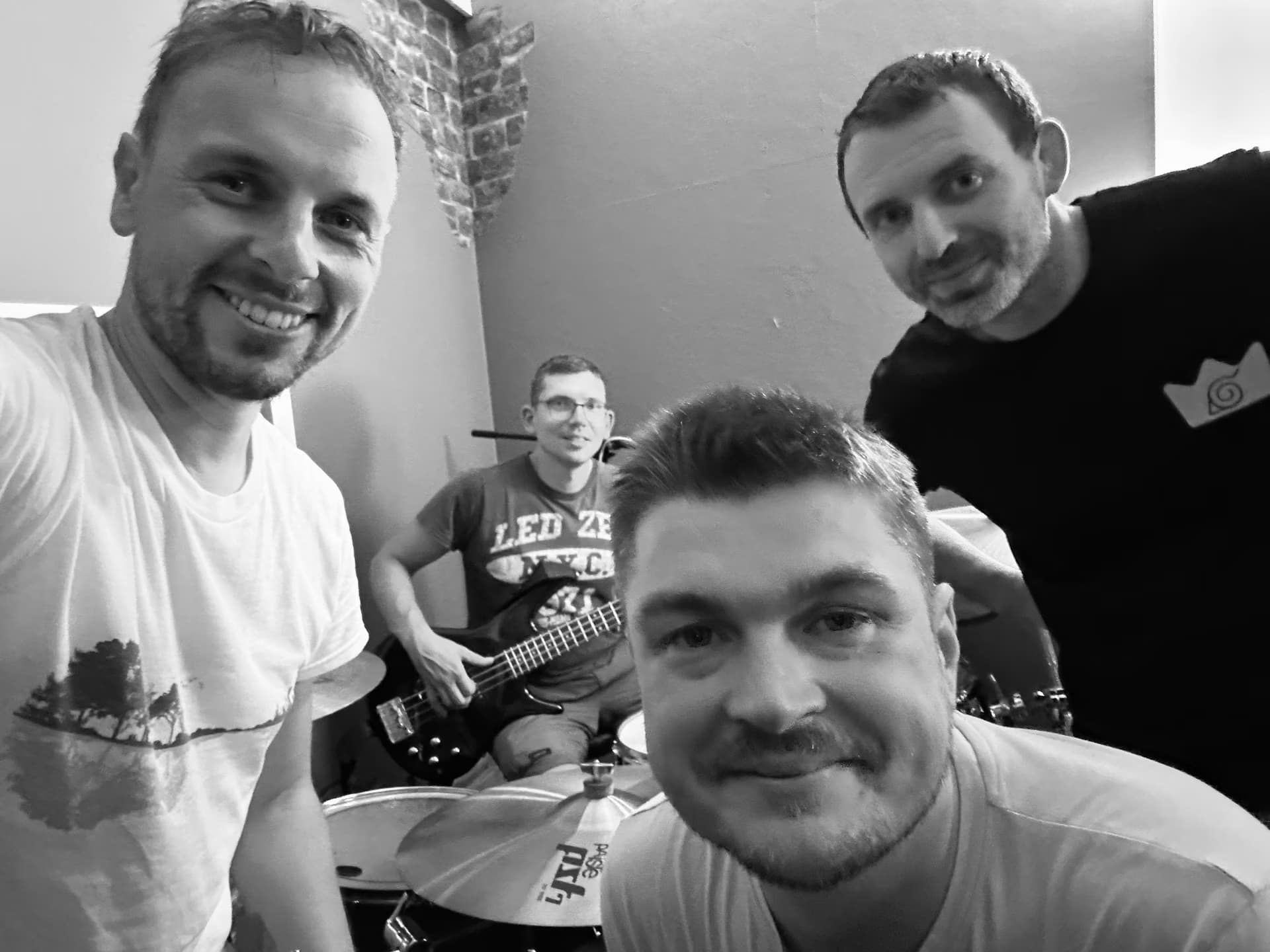 Czterech muzyków pozuje do wspólnego zdjęcia w studio z widoczną perkusją i gitarami.