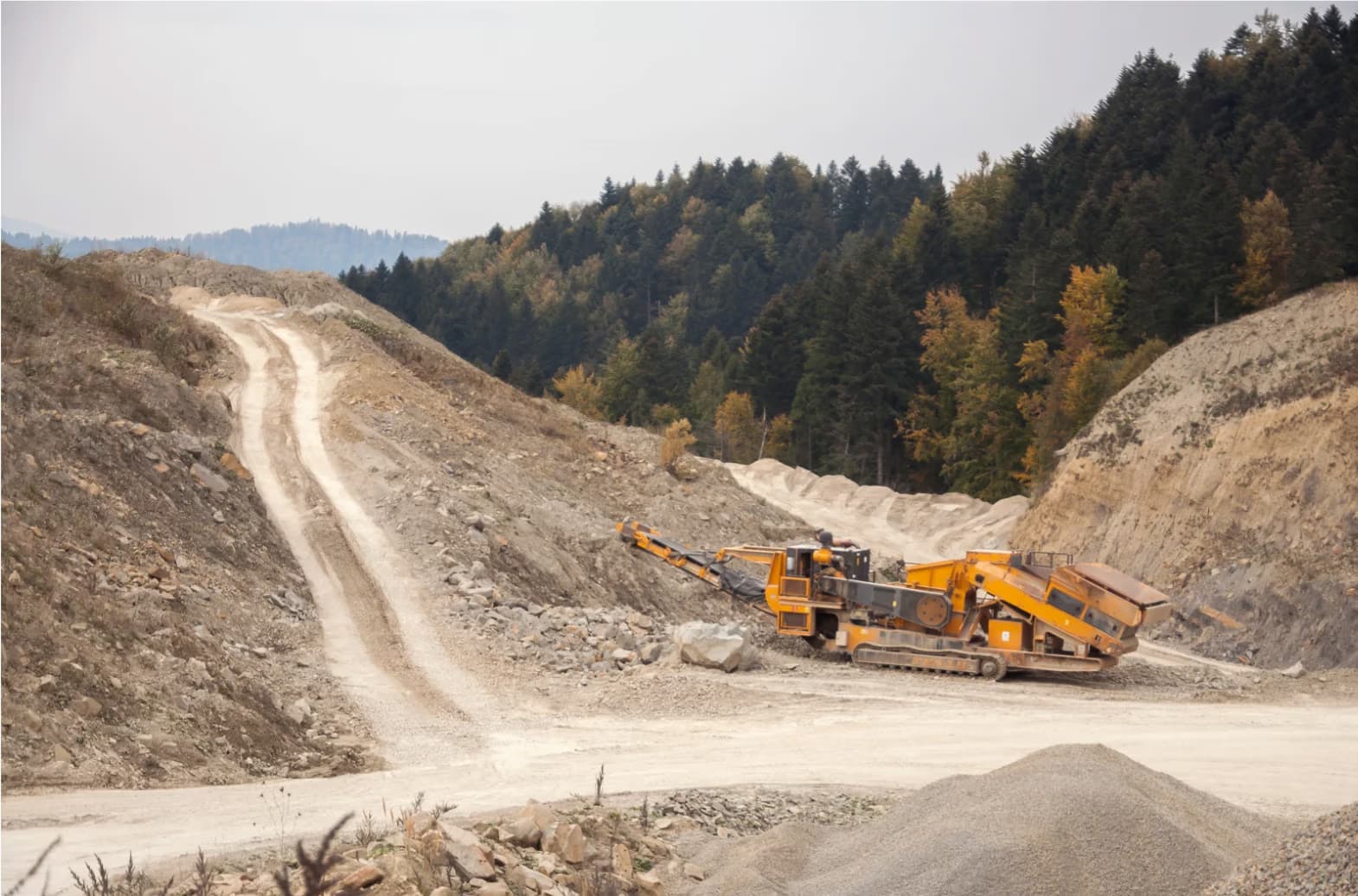 A large yellow heavy machinery crusher operates in a rocky open-pit stone quarry.