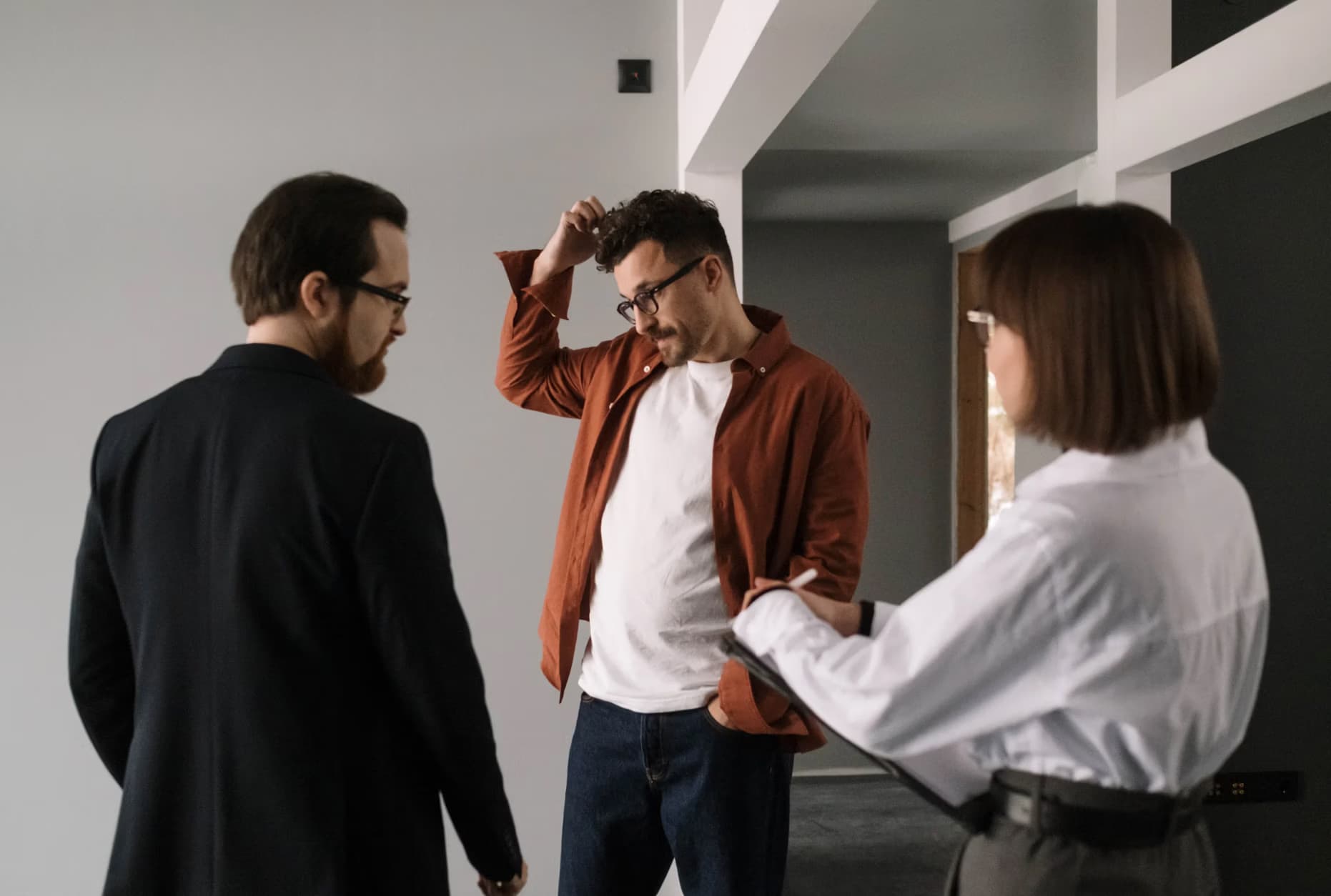 A man in a shirt stands between two people in an office during a business consultation.