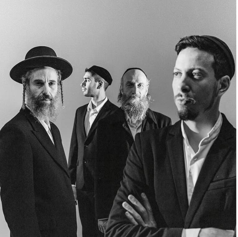 Four men in formal suits pose together against a plain grey studio background.