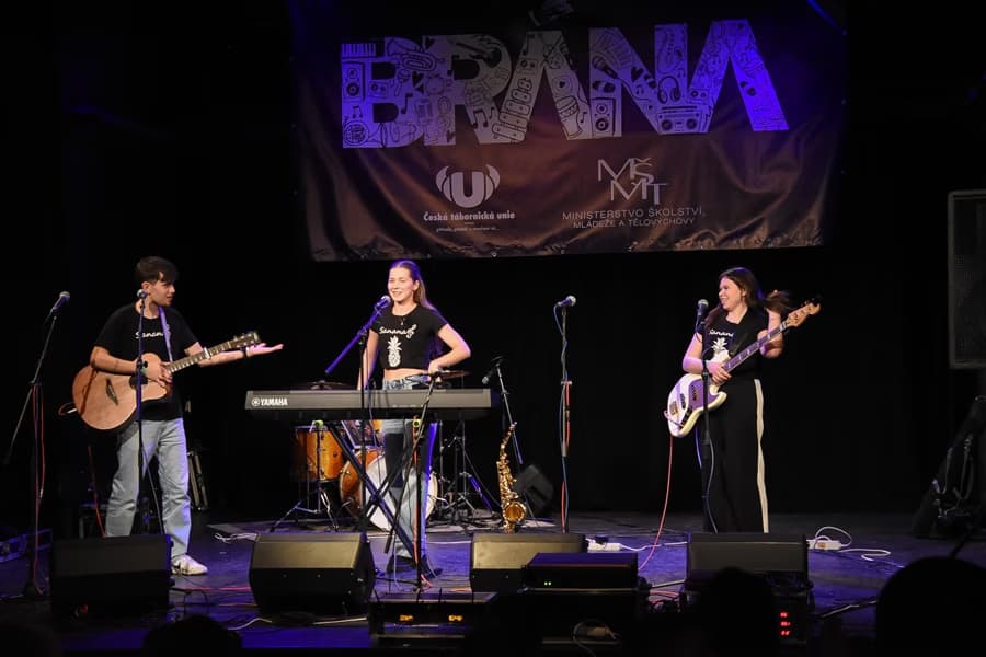 Three musicians perform on stage with instruments in front of a banner labeled BRANA.