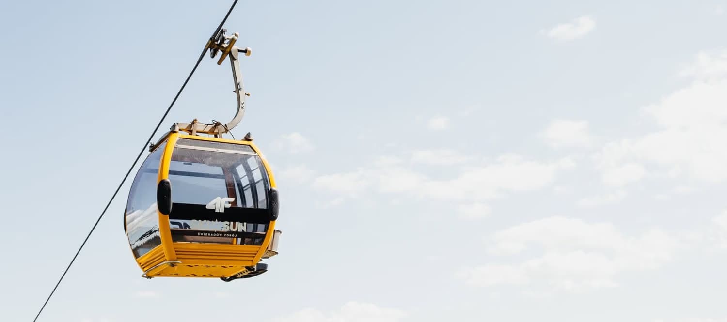 A single yellow cable car cabin suspended against a bright sky on a cable line.