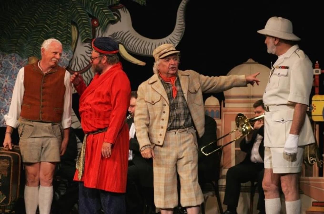 Vier Männer in Theaterkostümen treten vor einer Kulisse mit einem Elefanten auf.
