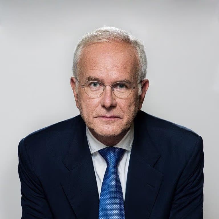 Portret dojrzałego mężczyzny z siwymi włosami, w okularach i granatowym garniturze.