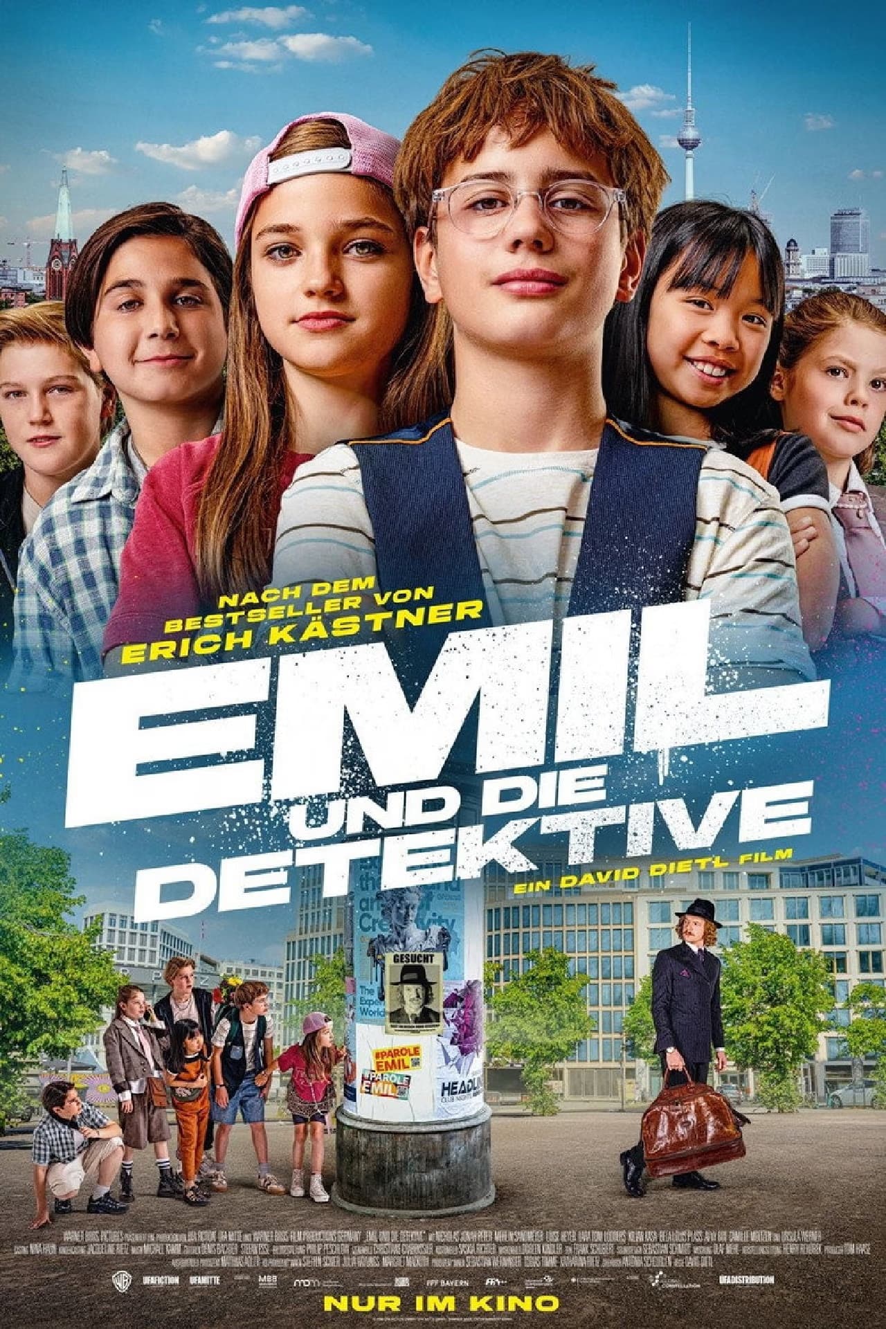 Eine Gruppe Kinder und ein Mann mit Koffer posieren vor der Kulisse der Stadt Berlin.
