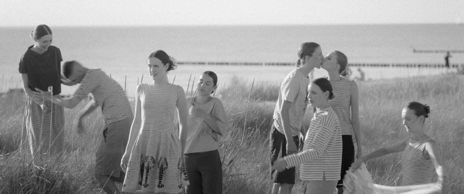 A group of people standing and moving through coastal dune grass near the sea.