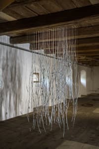 Art installation featuring many thin, white strings hanging from dark wooden ceiling beams indoors.